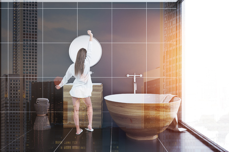 Rear view of a woman standing in a bathroom interior with black tiles and a loft window. Wooden tub and sink. 3d rendering toned image double exposureの写真素材