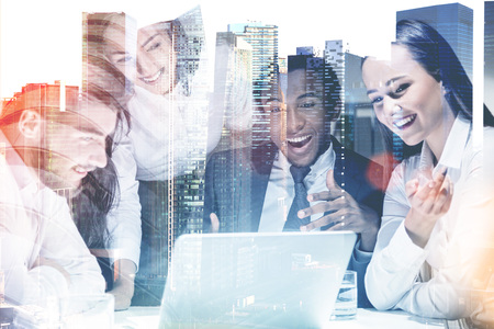 Members of a diverse business team sitting together at a table with a laptop. A cityscape background. Concept of start up success. Toned image double exposure mock up.の写真素材