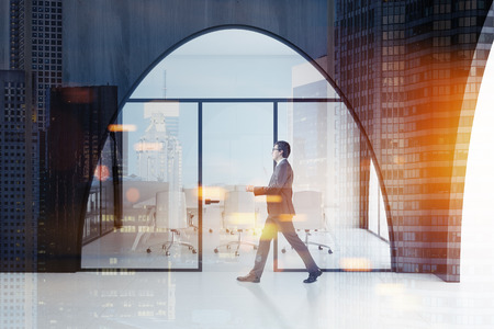 Businessman in a dark wooden office interior with a white floor, arched doorways and a long meeting room table with white chairs standing near it. 3d rendering mock up toned image double exposureの写真素材