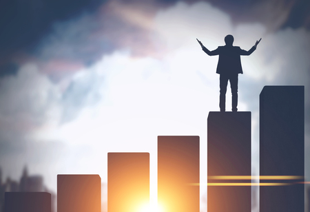 Silhouette of a young businessman standing on a bar chart against a big city sky background. Concept of business success. Toned image mock upの写真素材