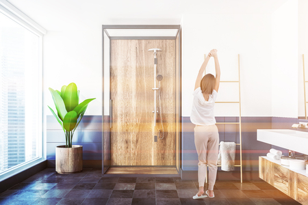 Wooden shower with a glass door standing in a white and blue wall bathroom with a panoramic window and a tiled floor. A woman 3d rendering toned imageの写真素材