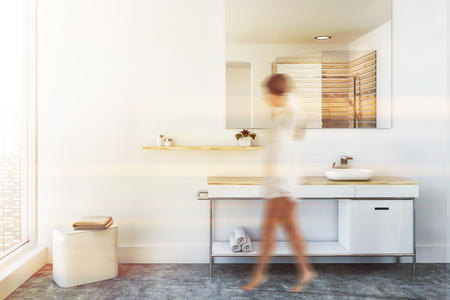 White sink vanity unit standing in a white wall room with a concrete floor. A panoramic window and a large mirror on the wall. A woman 3d rendering mock up toned image blurredの写真素材