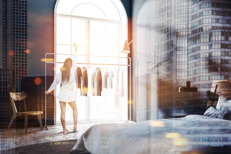 Woman in Scandinavian style bedroom with grey walls, a tiled floor, a clothes rack, and a master bed with bedside tables. Arched windows. 3d rendering mock up toned image double exposure cityの写真素材