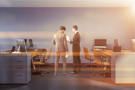 Office of a company manager with blue walls, a carpet on the floor, and stylish wooden computer tables. Two businessmen talking 3d rendering mock up toned imageの写真素材