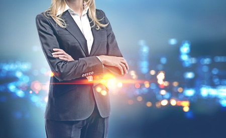 Unrecognizable confident businesswoman in suit standing with crossed arms over a night cityscape background. Toned image double exposure copy spaceの写真素材