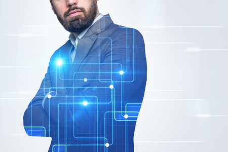 Unrecognizable bearded businessman standing with crossed arms in a white room with graphs holograms and hud. Hi tech concept. Toned image double exposure copy space film effectの写真素材