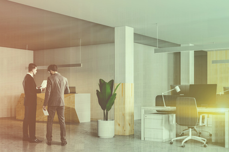 Two business people discussing company issues in office hall with wooden reception desk and glass walls. Toned image double exposureの写真素材