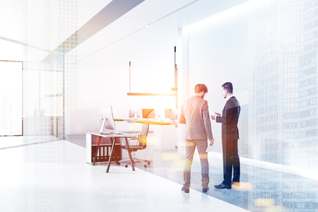 Two businessmen talking in minimalistic office interior with white walls, concrete floor with rows of white tables with black computer screens and panoramic windows. Toned image double exposureの写真素材