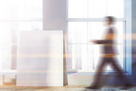 Man walking in empty room with gray walls, wooden floor and big windows with modern cityscape. Vertical mock up poster on the floor. Toned image blurredの写真素材