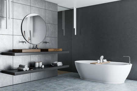 Interior of luxury bathroom with gray tile walls, concrete floor, white bathtub and double sink with...