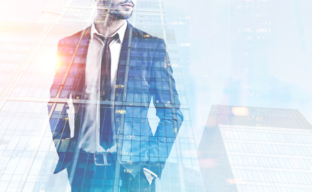 Unrecognizable bearded businessman standing with hands in suit pockets in modern city. Night cityscape double exposure. Business lifestyle concept. Toned image mock upの写真素材