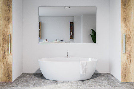 Modern bathroom interior with white walls, concrete floor, white bathtub with large mirror hanging...