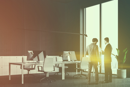 Businessmen talking in loft open space office with gray walls, carpet on the floor, rows of white computer tables with white chairs and white lockers. Toned imagedouble exposureの写真素材
