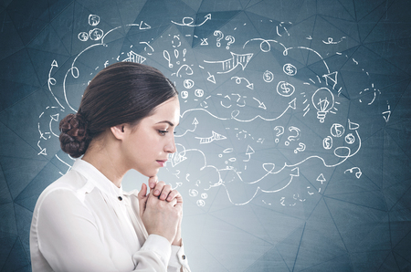 Side view of pensive young businesswoman with dark hair wearing white blouse sitting near geometric pattern wall with business plan sketch.の写真素材