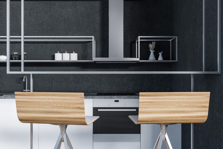Two wooden stools near bar table in modern kitchen interior with black walls, white countertops with...