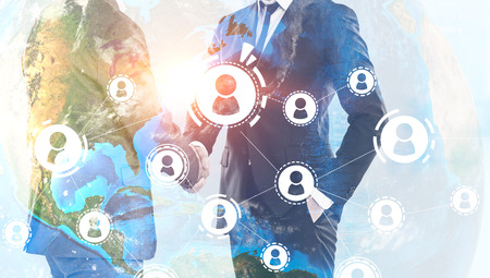 Unrecognizable businessmen shaking hands over Earth background with people network hologram. Toned image double exposure Elements of this image furnished by NASAの写真素材