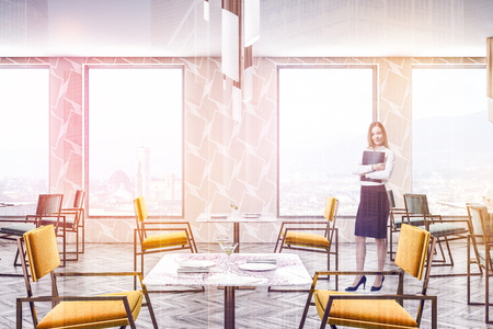 Woman in modern restaurant interior with beige geometric pattern walls, wooden floor and green and yellow chairs standing near square tables. Toned imageの写真素材