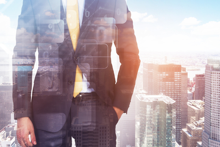 Unrecognizable businessman standing with hand in pocket over modern cityscape background with double exposure of digital interface. Toned image double exposureの写真素材