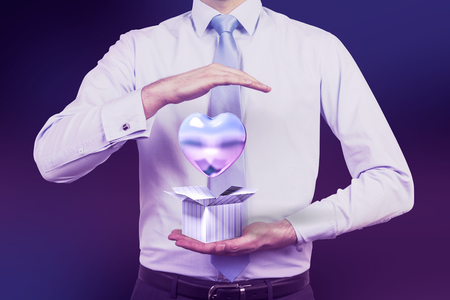 Unrecognizable young man in shirt and tie holding striped blue present box with blue heart balloon flying out of it. Concept of love. Toned imageの写真素材