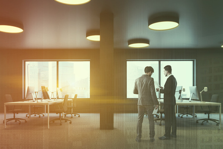 Side view of industrial style office with brown walls, carpet on the floor, columns and rows of white computer tables with brown chairs. Windows with cityscape. Businessmen Toned image double exposureの写真素材