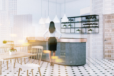 Woman in corner of bar with white brick walls, tiled floor, gray bar, shelves with wines and wooden tables with white and wooden chairs. Toned image double exposureの写真素材