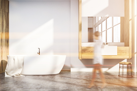 Woman in interior of modern bathroom with white and wooden walls, concrete floor, white bathtub and sink standing on wooden countertop. Toned image blurの写真素材