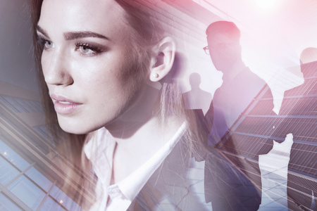 Portrait of beautiful woman business leader with her team members silhouettes over skyscrapers background. Toned image double exposureの写真素材