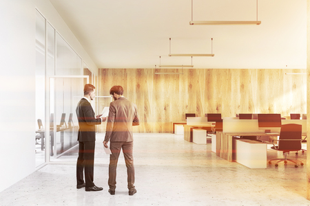 Businessmen in interior of modern office with white and wooden walls, concrete floor, white and wooden computer tables and black chairs. Toned imageの写真素材