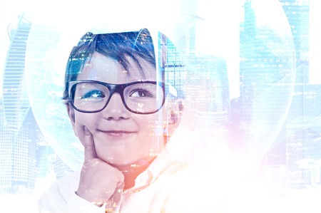 Adorable thinking little boy wearing glasses over cityscape background with Earth hologram.の写真素材