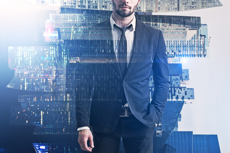 Unrecognizable bearded businessman standing with his hand in pocket over day and night city background. Toned image double exposureの写真素材