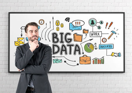 Portrait of pensive young caucasian businessman with beard wearing dark suit standing near whiteboard with colorful big data sketch on itの写真素材