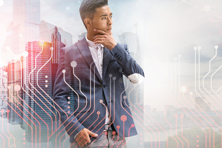 Portrait of thoughtful Asian businessman standing over modern cityscape background with double exposure of circuits. Concept of hi tech in business. Toned imageの写真素材