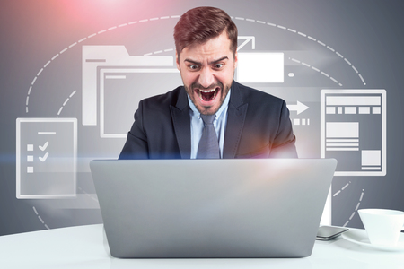 Stressed bearded businessman looking at his laptop and shouting. Electronic documents interface behind him. Concept of paperwork overloadの写真素材