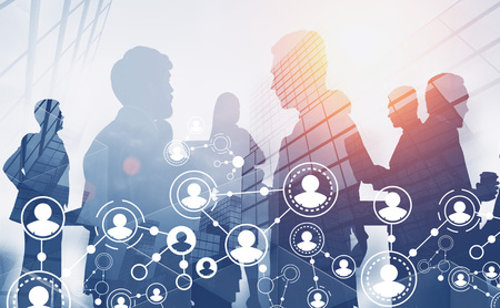 Silhouettes of business team members working together over skyscraper background with double exposure of social network hologram. HR concept. Toned imageの写真素材