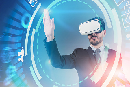 Serious young businessman with beard wearing suit and vr glasses working with hud internet...