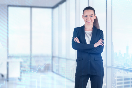 Smiling young businesswoman in dark suit standing with crossed arms in panoramic office with double exposure of graphs. Toned imageの写真素材