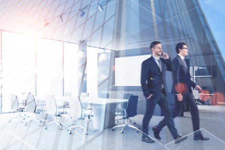Two young businessmen walking in modern office meeting room with double exposure of skyscraper. Concept of business lifestyle. Toned image blurredの写真素材