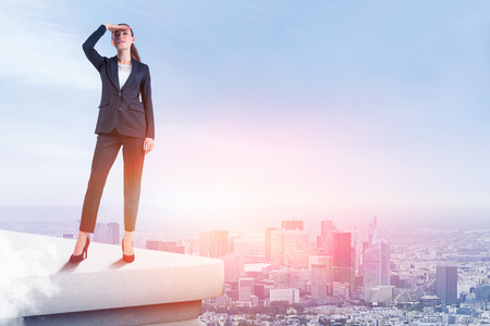 Young businesswoman in dark suit looking forward standing on rooftop over cityscape background. Concept of future of business. Toned imageの写真素材