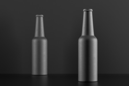 Two closed black matt bottles standing on black table over gray background. 3d renderingの写真素材