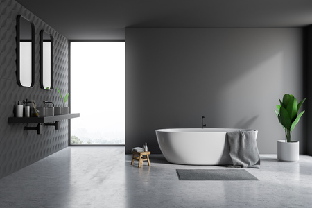 Interior of bathroom with gray and tiled walls, concrete floor, white bathtub with towel on it and double sink standing on gray countertop with two vertical mirrors. 3d renderingの写真素材