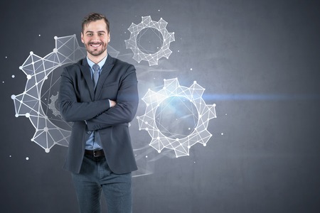 Portrait of smiling businessman wearing black suit standing with crossed arms near concrete wall with gears drawn on it. Concept of teamwork. Mock upの写真素材