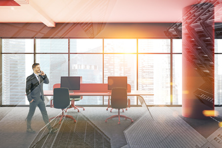 Businessman with phone in interior of open space office with gray walls, pink ceiling and columns, panoramic windows, pink and glass computer tables and green chairs. Toned image double exposureの写真素材