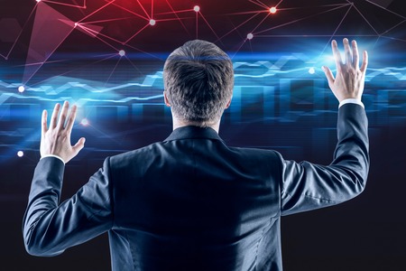 Rear view of young businessman working with graphs and network interface over dark blue background. Concept of hi tech. Toned imageの写真素材