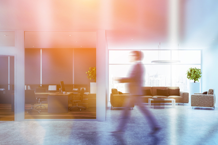 Businessman in interior of manager office with blue and white walls and lounge room with beige armchairs and sofa sanding near white and glass coffee table. Toned image blurredの写真素材