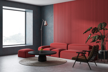 Corner of modern living room with concrete and red walls, concrete floor, comfortable red sofa and...