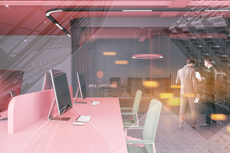 Two businessmen discussing work in modern open space office with gray walls, concrete floor, rows of pink computer tables with green chairs and glass wall meeting room. Toned image double exposureの写真素材