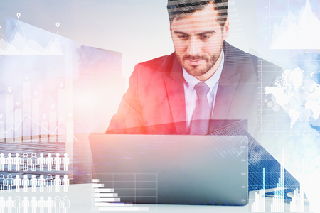Serious young businessman looking at laptop with double exposure of global business interface. Skyscrapers background. Toned image. Elements of this image furnished by NASAの写真素材