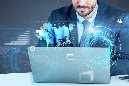 Unrecognizable young businessman looking at laptop with double exposure of global business interface and HUD. Toned image. Elements of this image furnished by NASAの写真素材
