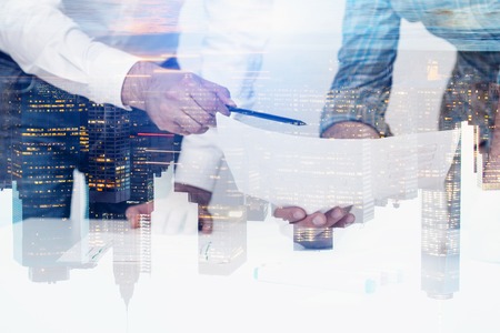 Hands of business people discussing documents with double exposure of night cityscape. Concept of...