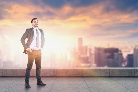 Confident young businessman standing on skyscraper roof with blurred city in background. Concept of leadership. Toned imageの写真素材